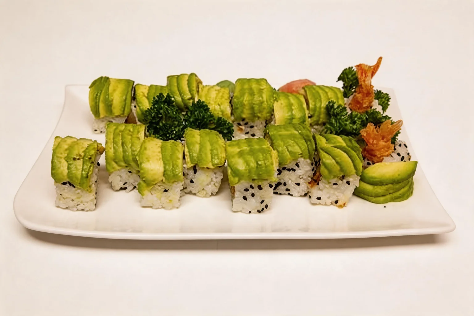 Rolls topped with thin slices of avocado, on a white plate with tempura shrimp on the side