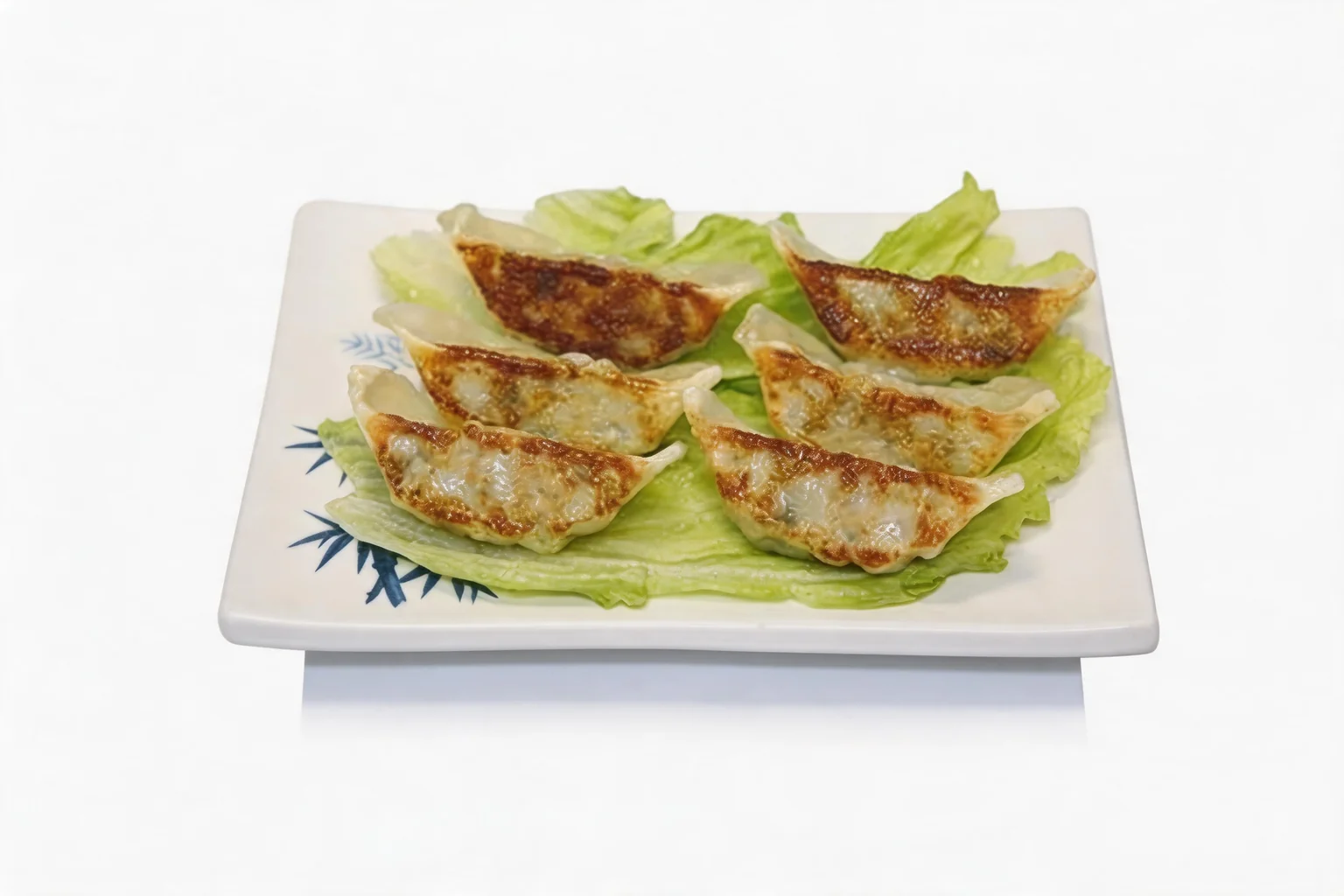 Six grilled gyoza on a bed of lettuce, on a white plate with a bamboo motif