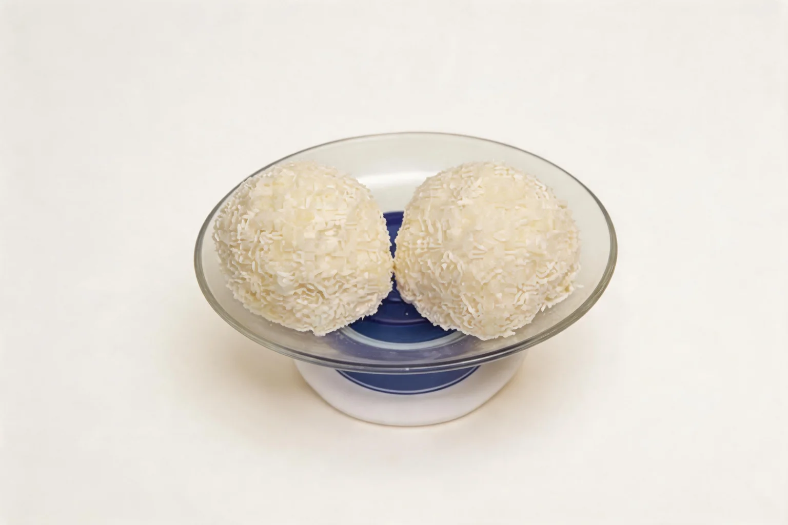 Two balls coated in grated coconut, served in a small blue glass bowl